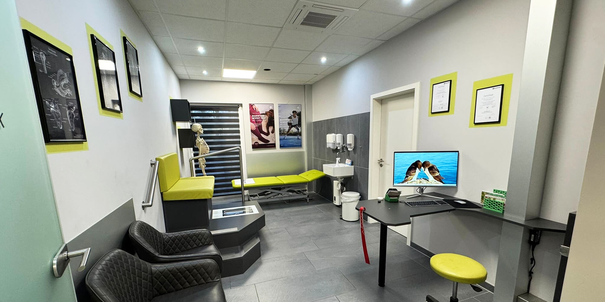 Behandlungsraum mit höhenverstellter Therapieliege, Sitzgelegenheiten und medizinischer Ausstattung