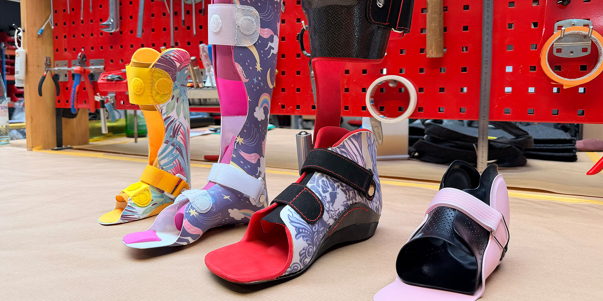 Verschiedene individuell angepasste Kinderorthesen in unterschiedlichen Farben und Designs auf einer Werkbank in der Orthopädietechnik-Werkstatt